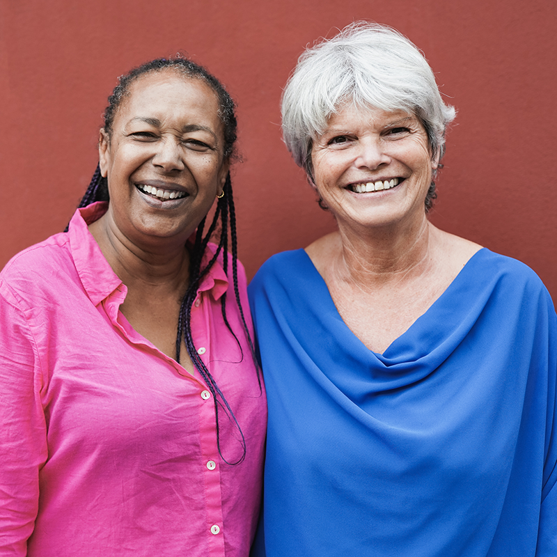 Two women standing next to one another smiling at the camera