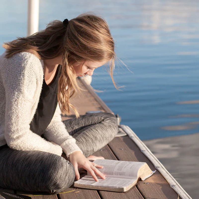 Young woman reading a bible next to a river